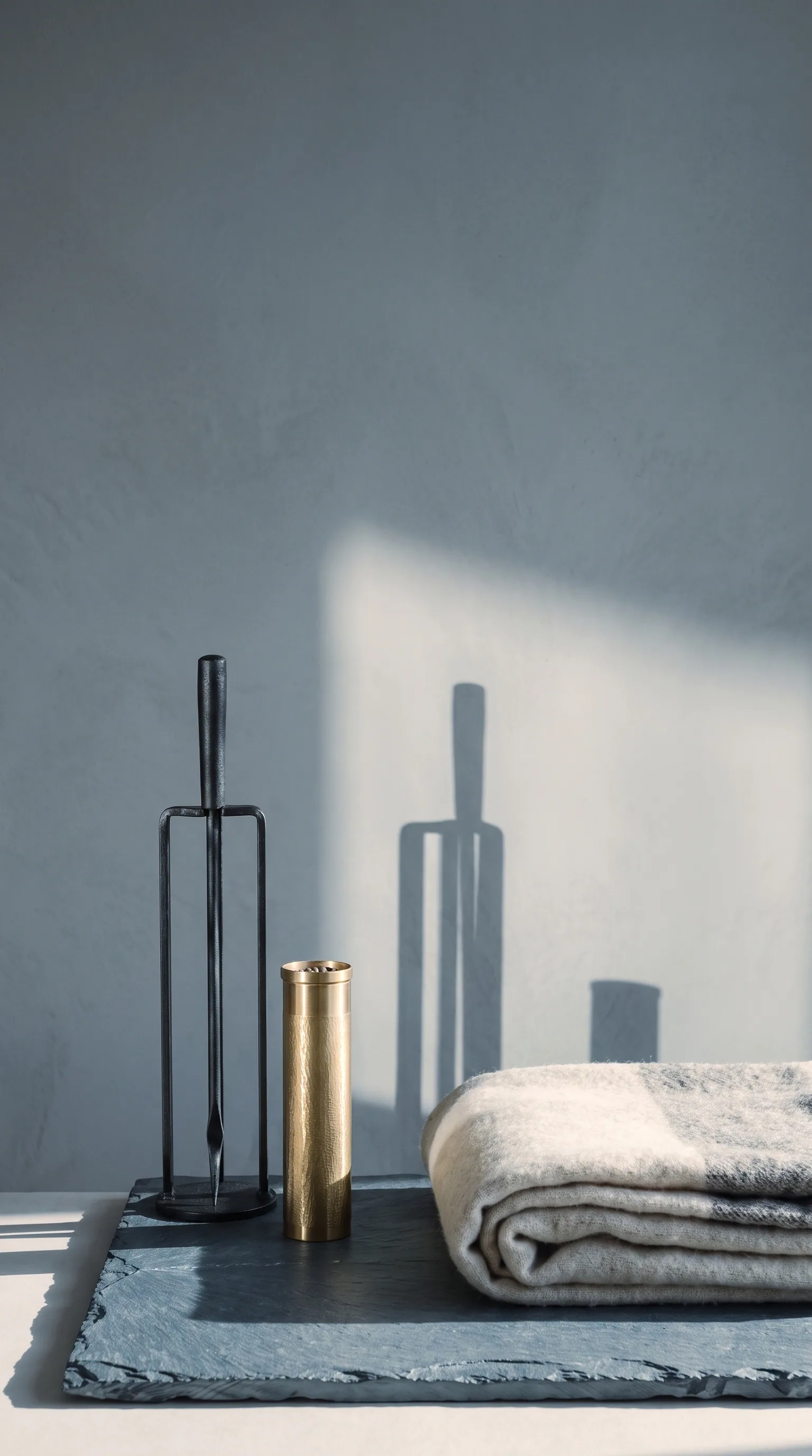 Hearth tools, a brass match safe and a folded wool blanket on a slate hearth.
